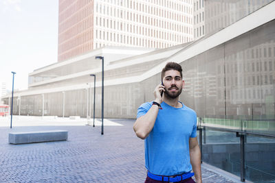 Smiling man talking on phone while standing against building