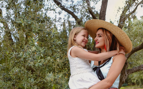 Happy mother holding daughter while standing against tree