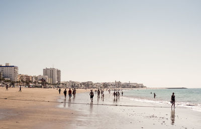 People walking on beach against clear sky