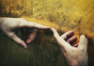 Cropped hands of friends touching by golden wall