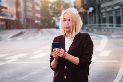 Young woman using phone while standing on street in city