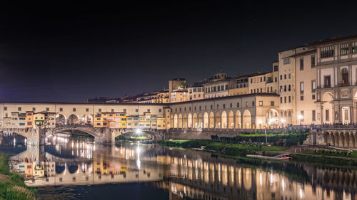 Bridge over river against buildings in city at night