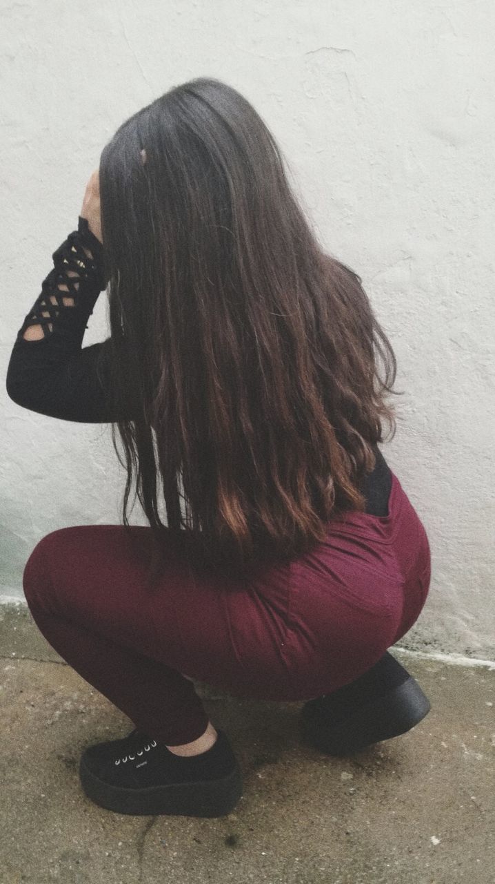 one person, hair, long hair, real people, hairstyle, lifestyles, women, sitting, full length, fashion, leisure activity, crouching, adult, shoe, wall - building feature, day, young women, casual clothing, indoors, teenager