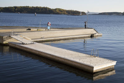 Distance view of man standing on pier over lake against sky