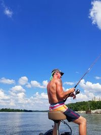 Side view of shirtless man fishing by lake