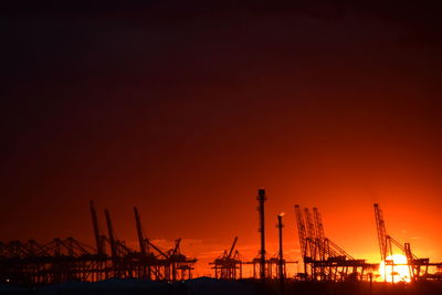 Silhouette cranes at commercial dock against sky during sunset