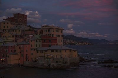 Buildings by sea against sky at sunset