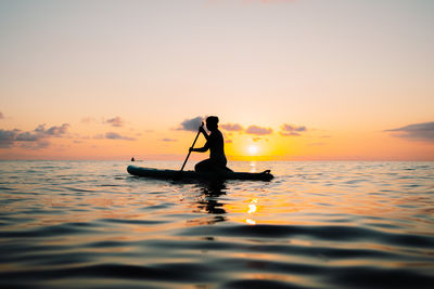 Silhouette man rowing in sea against sky during sunset