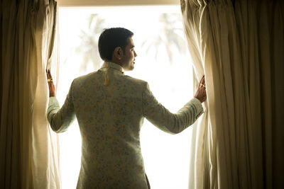 Rear view of woman standing by window at home