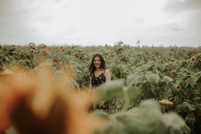 Young woman standing amidst sunflowers on field