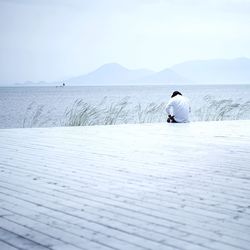 Rear view of person sitting by sea against clear sky