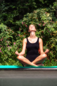 Young woman meditating while sitting against plants