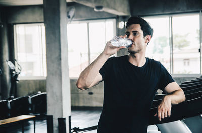 Thoughtful young man drinking water while standing in gym
