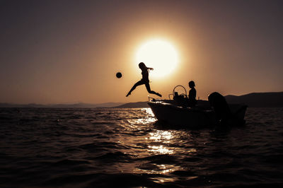 Silhouette people on sea against sky during sunset