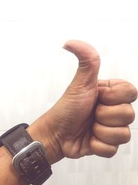 Close-up of hand holding clock against white wall