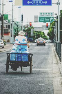 Rear view of man carrying water bottles on vehicle at street