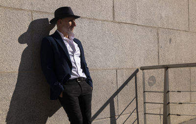 Portrait of adult man in hat and suit standing on street against wall. madrid, spain