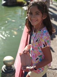 Portrait of smiling girl holding paper bag while standing by railing