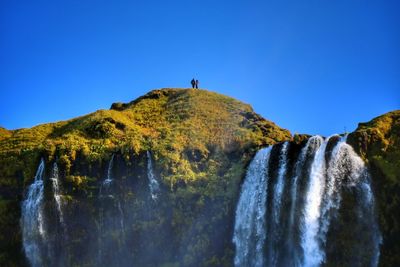 Low angle view of waterfall against clear blue sky