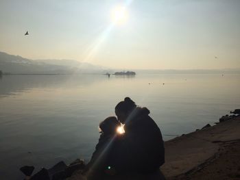 Mother and daughter kissing by lake against sky on sunny day