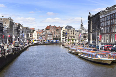 Boats moored in canal amidst buildings in city against sky