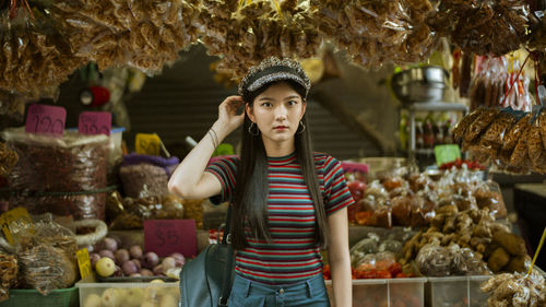 Portrait of beautiful young woman standing against market stall