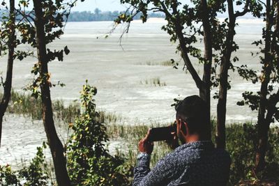 Rear view of man photographing dried field during draught