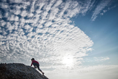 Side view of boy climbing mountain against cloudy sky
