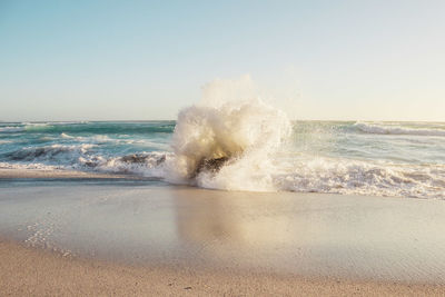 Waves splashing on shore against clear sky