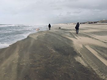 People walking at beach against sky