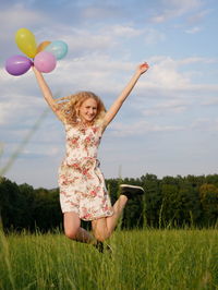 Full length of woman with arms raised on field against sky