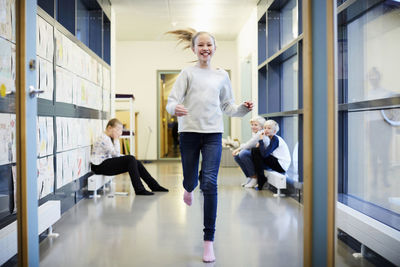 Smiling girl running in school corridor with friends in background