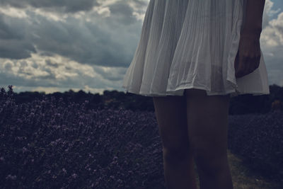 Midsection of woman standing in field against cloudy sky