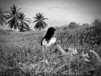 Woman sitting on field by trees against sky