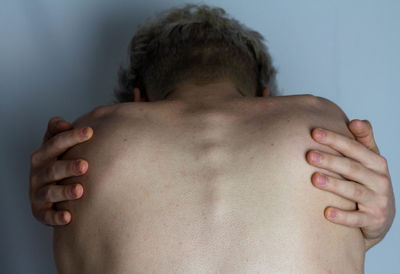 Rear view of shirtless man hugging self against white background