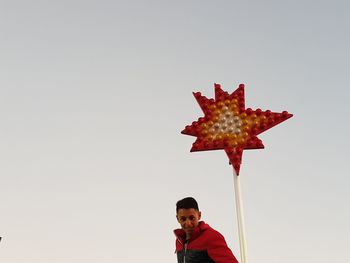 Portrait of young man holding maple leaf against clear sky