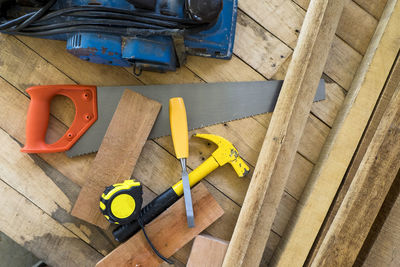 Directly above shot of hammer with hand saw and tape measure on wooden plank