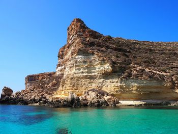 Rock formations by sea against clear blue sky