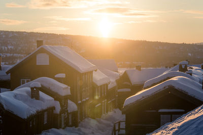 Snow covered houses and buildings against sky during sunset