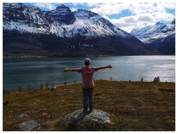 Rear view of boy standing on lake against mountain range