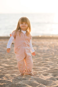 Smiling pretty little child 2-3 year old play at beach over sea at background in sun light outdoors