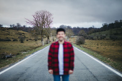 Anonymous blurred man in casual wear walking on empty asphalt road among green fields with cloudy sky on background