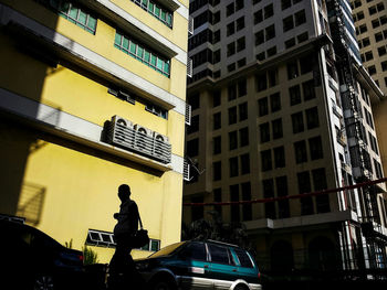 Low angle view of silhouette man walking against yellow building in city
