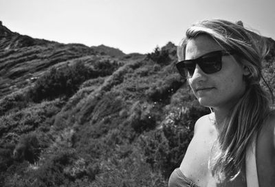 Young woman wearing sunglasses standing against hill