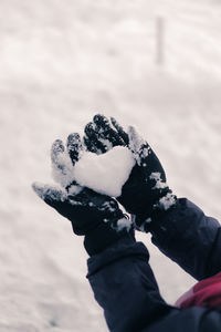 Close up of a kid forming a heart out of snow and holding it in hands,  showing  love for winter.