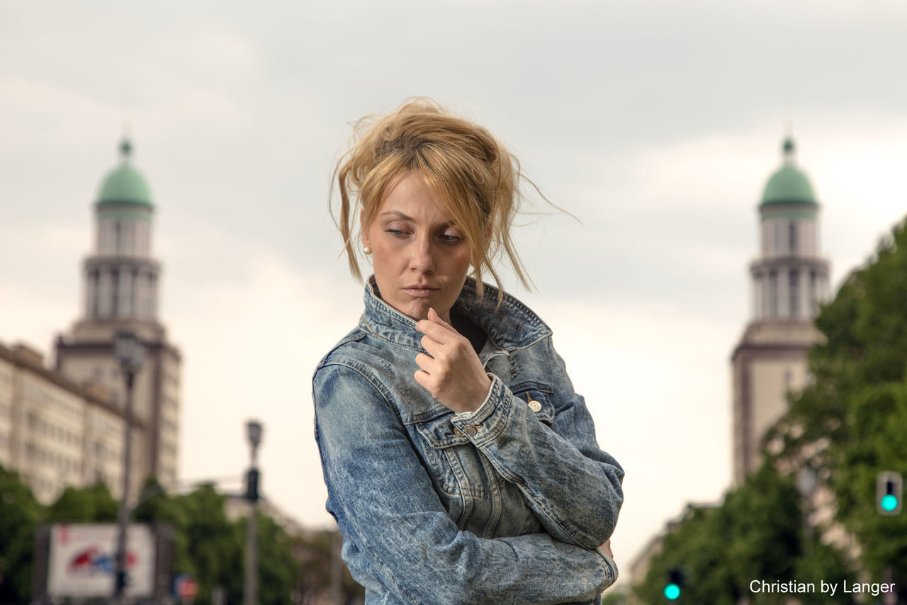 architecture, building exterior, built structure, focus on foreground, lifestyles, person, casual clothing, young adult, portrait, leisure activity, city, sky, smiling, looking at camera, standing, tower, waist up