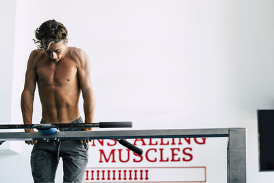 Shirtless boy exercising while standing against wall