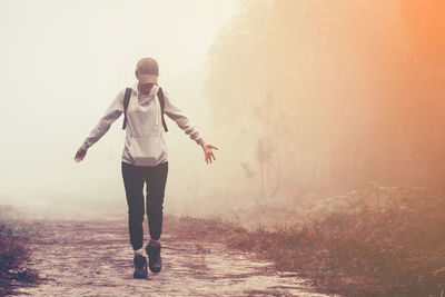 Young woman with arms outstretched walking in forest during foggy weather