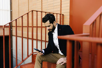 Young man using mobile phone while sitting on staircase