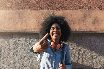 Portrait of happy young woman gesturing while standing against wall